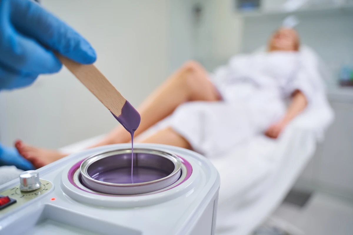 patyczek zamoczony w fioletowym płynie na tle leżącej kobiety czekającej na zabieg depilacji