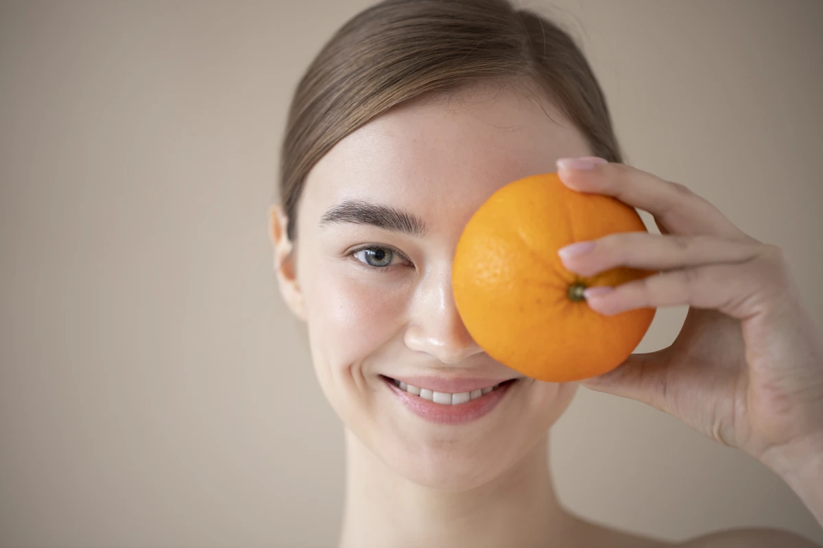 młoda kobieta zasłania lewe oko pomarańczą
